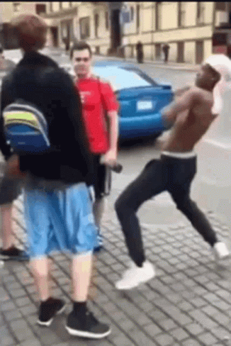 A Group Of Men Are Standing On A Brick Sidewalk Fighting Each Other . GIF