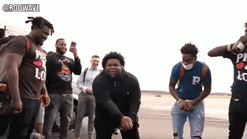 A Group Of Men Are Standing On A Street And One Of Them Is Wearing A Shirt That Says Rodwave GIF