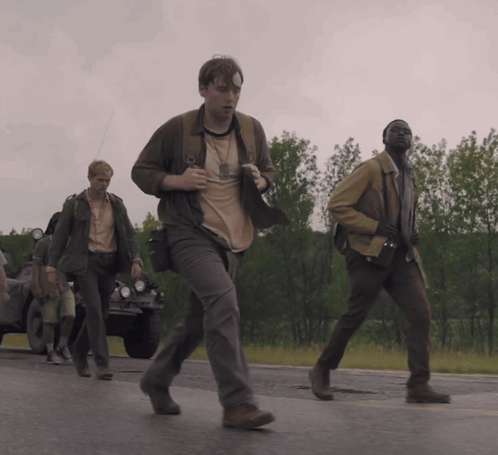 A Group Of Men Are Walking Down A Road And One Of Them Has A Badge On His Chest GIF