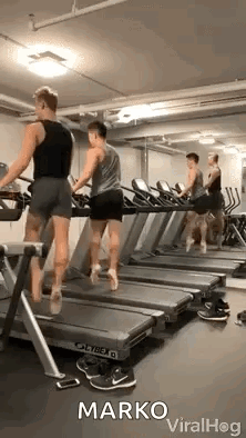 A Group Of Men Are Walking On Treadmills In A Gym . GIF