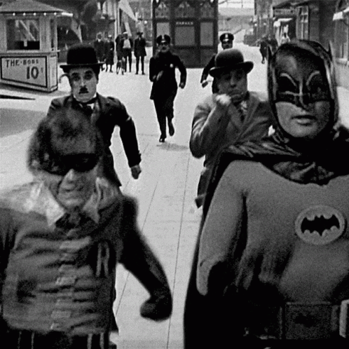 A Group Of Men Dressed As Batman And Robin Are Walking Down The Street GIF