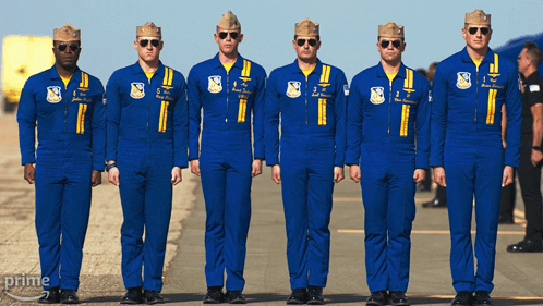 A Group Of Men In Blue Jumpsuits Are Standing In A Line With The Word Prime On The Bottom Right GIF