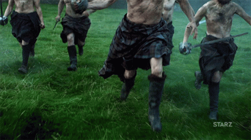 A Group Of Men In Kilts Are Running Through A Grassy Field With The Starz Logo In The Corner GIF