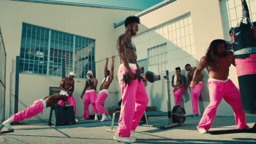 A Group Of Men In Pink Sweatpants Are Doing Exercises In Front Of A Building GIF