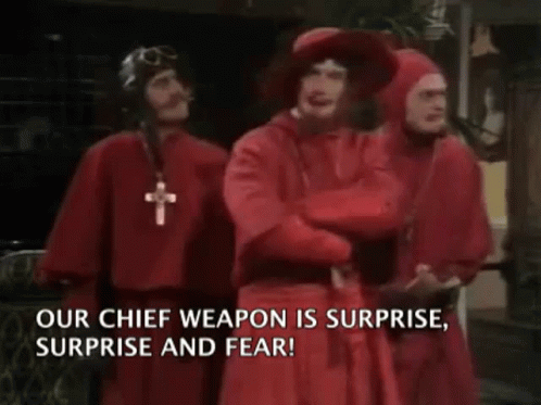 A Group Of Men In Red Robes Are Standing Next To Each Other With The Words " Our Chief Weapon Is Surprise Surprise And F GIF
