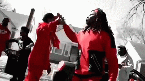 A Group Of Men In Red Shirts Are Dancing In Front Of A Building . GIF
