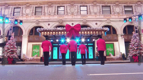 A Group Of Men In Red Uniforms Are Dancing In Front Of A Building That Says Nbc On The Front GIF