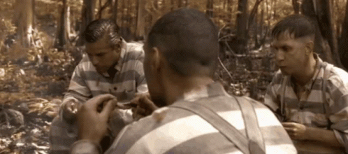 A Group Of Men In Striped Shirts Are Sitting In A Forest GIF
