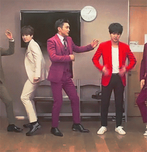 A Group Of Men In Suits And Jackets Are Dancing In Front Of A Clock GIF
