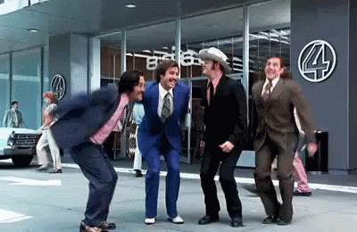 A Group Of Men In Suits And Ties Are Dancing On The Sidewalk In Front Of A Store . GIF