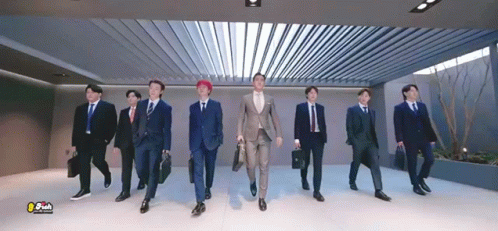 A Group Of Men In Suits And Ties Are Walking In A Hallway . GIF