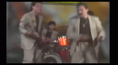 A Group Of Men In Suits Are Dancing In Front Of A Drum Set In A Room . GIF