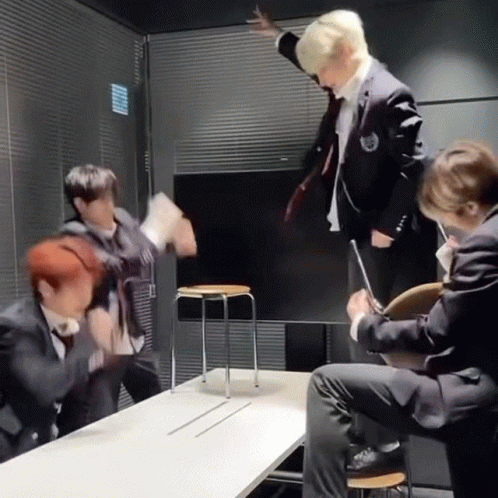 A Group Of Men In Suits Are Sitting Around A Table And A Man Is Standing On A Chair . GIF