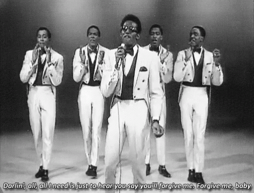 A Group Of Men In Tuxedos Are Singing Into Microphones . GIF