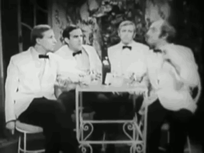 A Group Of Men In Tuxedos Are Sitting At A Table Talking To Each Other . GIF