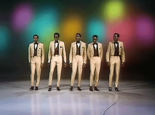 A Group Of Men In Tuxedos Are Standing In A Line GIF