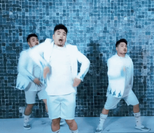 A Group Of Men In White Clothes Are Dancing In Front Of A Blue Tiled Wall GIF