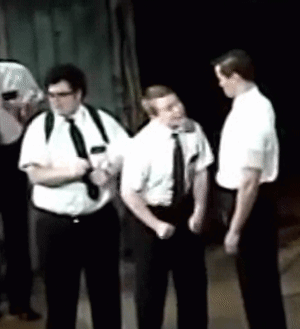 A Group Of Men In White Shirts And Black Ties Are Standing In A Dark Room GIF