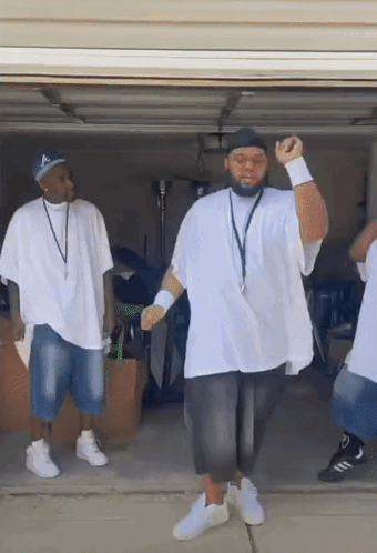 A Group Of Men In White Shirts Are Dancing In A Garage Doorway . GIF