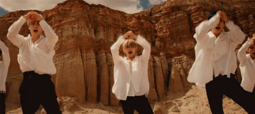 A Group Of Men In White Shirts Are Dancing In Front Of A Rocky Mountain GIF