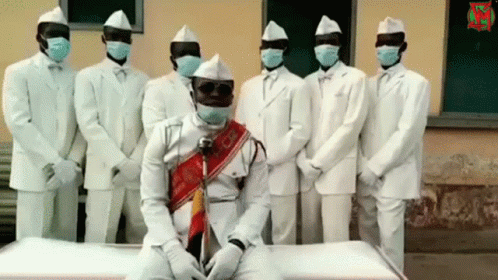 A Group Of Men In White Suits And Hats Are Standing Around A Coffin GIF