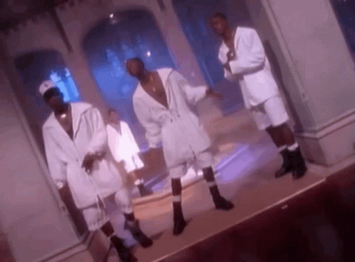 A Group Of Men In White Suits And Socks Are Dancing On A Stage In A Room . GIF
