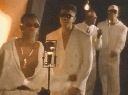 A Group Of Men In White Suits And Sunglasses Are Standing Next To Each Other In Front Of A Microphone . GIF