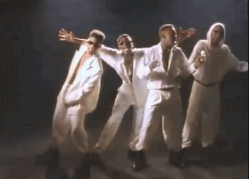 A Group Of Men In White Suits Are Dancing Together On A Stage In A Dark Room . GIF