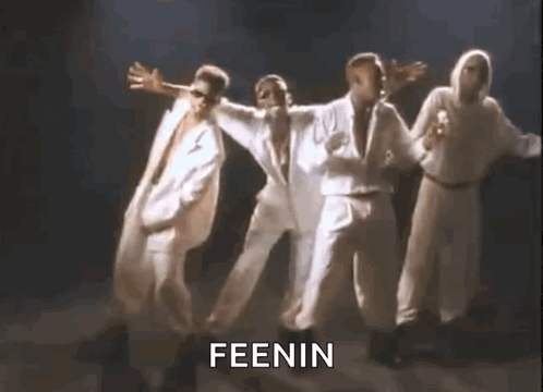 A Group Of Men In White Suits Are Dancing Together On A Stage In A Dark Room . GIF