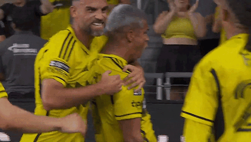 A Group Of Men In Yellow Jerseys Are Hugging Each Other . GIF