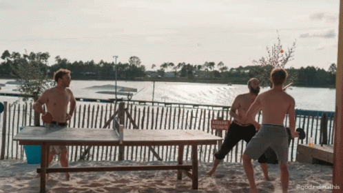A Group Of Men Playing Ping Pong On A Beach With A Sign In The Background That Says " Attention Vehicule " GIF