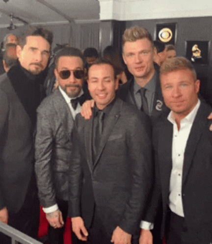 A Group Of Men Posing For A Picture With One Wearing Sunglasses And A Grammy Plaque Behind Them GIF