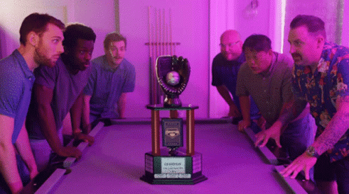A Group Of Men Stand Around A Pool Table With A Trophy That Says Champions GIF