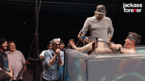 A Group Of Men Standing Around A Man In A Tank With The Words Jackass Forever On The Bottom GIF