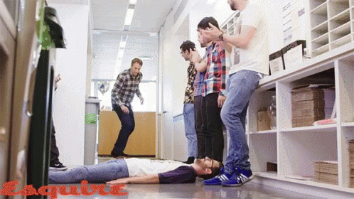 A Group Of Men Standing Around A Man Laying On The Floor With Esquire Written On The Bottom Right GIF