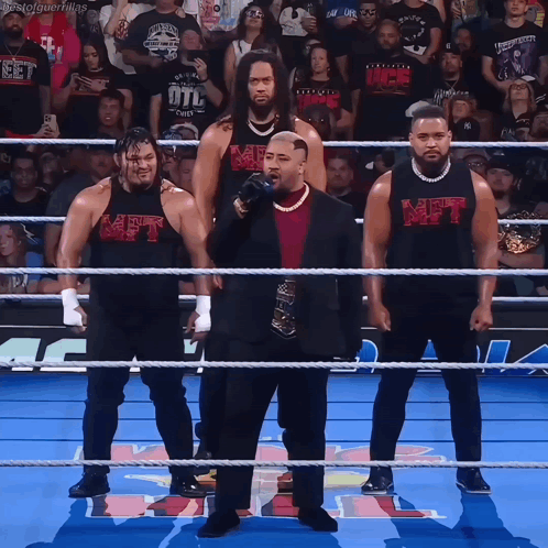 A Group Of Men Standing In A Wrestling Ring With One Wearing A Shirt That Says Met On It GIF