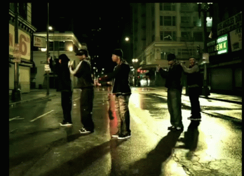 a group of men standing on a wet street in front of a sign that says emm