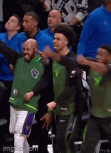 A Group Of Men Wearing Green And Black Jerseys Are Dancing In A Stadium GIF