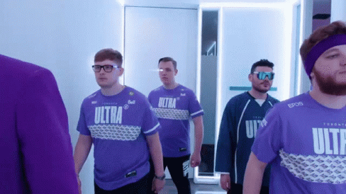 A Group Of Men Wearing Purple Ultra Shirts Are Walking Down A Hallway GIF
