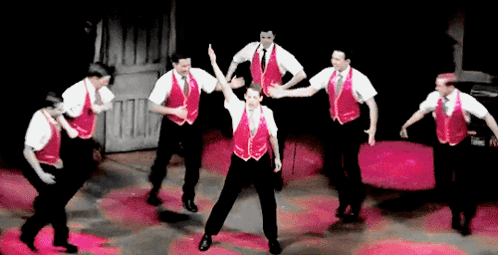 A Group Of Men Wearing Red Vests And White Shirts Are Dancing On A Stage GIF