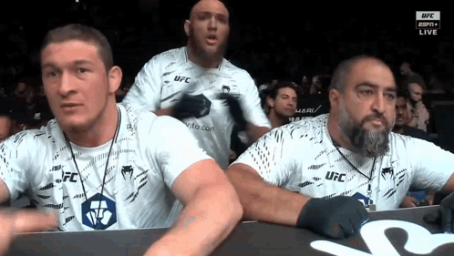 A Group Of Men Wearing White Ufc Shirts Are Watching A Fight GIF