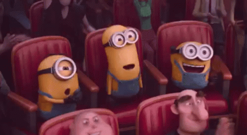 A Group Of Minions Are Sitting In A Row Of Red Chairs In A Theater . GIF