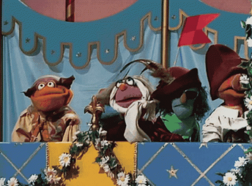 A Group Of Muppets Are On A Stage With Flowers And A Flag In The Background GIF
