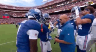 A Group Of New York Giants Football Players Are Standing On A Field Talking To Each Other . GIF