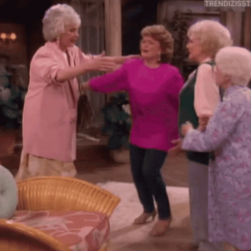 A Group Of Older Women Are Dancing In A Living Room . One Of The Women Is Wearing A Pink Sweater . GIF