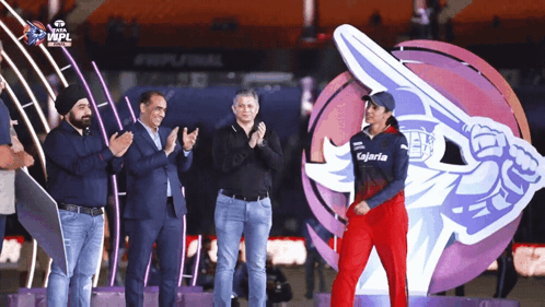 A Group Of People Applaud A Woman Wearing A Kalaria Shirt GIF