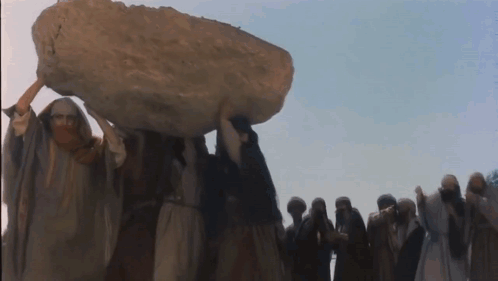 A Group Of People Are Carrying A Large Rock On Their Heads GIF