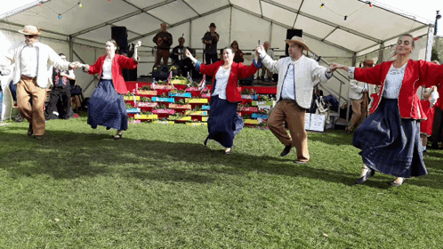 A Group Of People Are Dancing In A Field In Front Of A Tent GIF