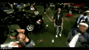 a group of people are dancing in a parking lot with cars in the background .