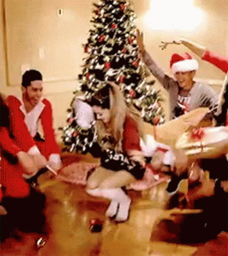 A Group Of People Are Dancing In A Room In Front Of A Christmas Tree . GIF